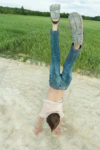 Gymnastic handstand of teenage boy on dirt road at green farm field background outdoors