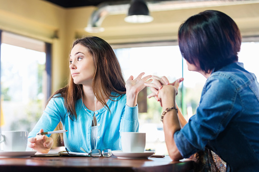 Annoyed teen girl talking to mother in coffee shop