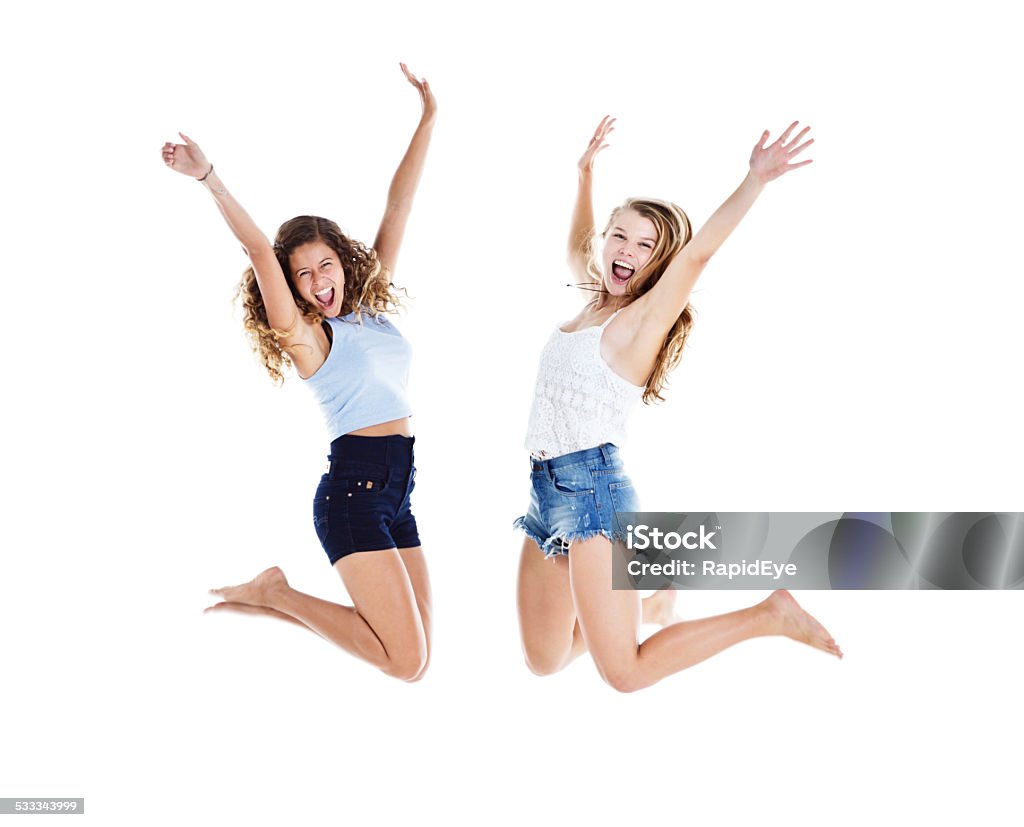 Jumping for joy! Two young beauties leap up, laughing Two pretty, smiling young women jump energetically into the air, laughing and gesturing joyfully. Isolated on white. 20-29 Years Stock Photo