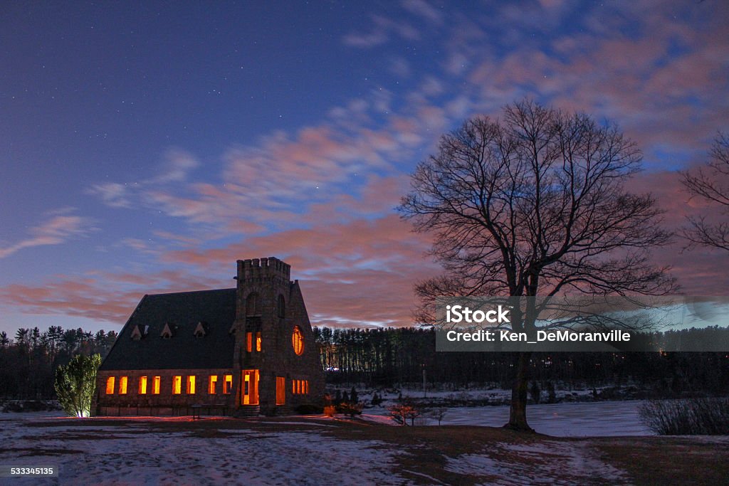 Winter sunset with lighted church with snow cover. Winter scene at sunset.  The warm glow through church windows. Snow cover on the shore of a frozen lake. 2015 Stock Photo