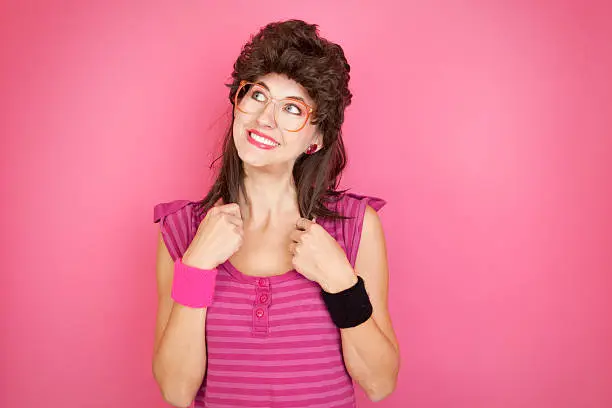 A smiling 80's styled woman with a mullet and big glasses.