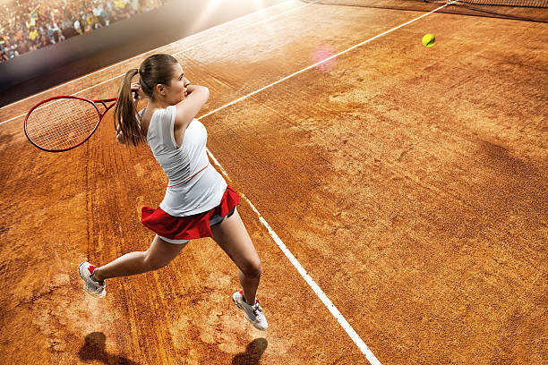 Female tennis player in action Focus is on the woman's jump ready to give back a ball with a tennis racket. The tennis player is in a tennis match in a generic outdoor tennis arena full of spectators. Tennis Player wears a generic unbranded tennis sport-cloth. wimbledon stock pictures, royalty-free photos & images