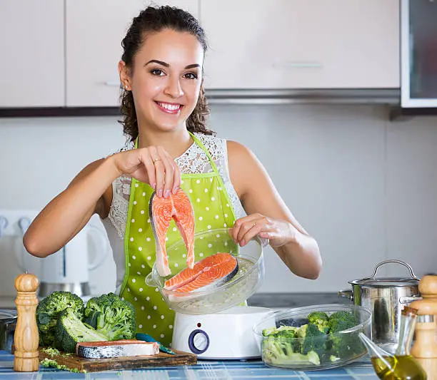 Portrait of smiling girl preparing fish and veggies in steamer