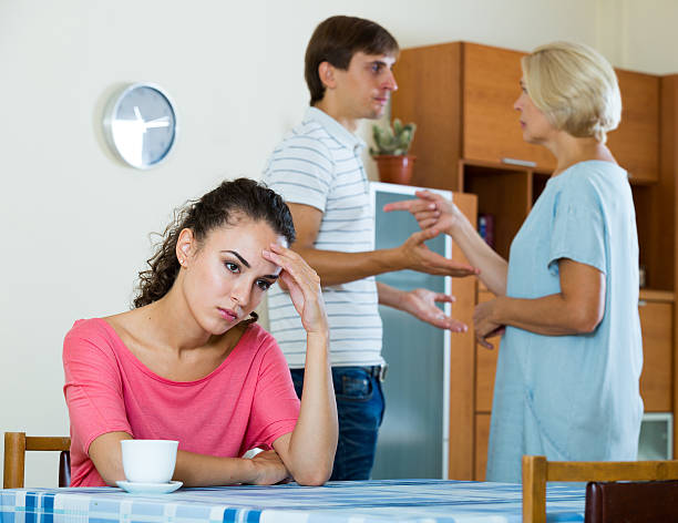 Sad young woman watching husband and mother having fight Upset girl apart from her husband and senior mother quarrelling mother in law stock pictures, royalty-free photos & images
