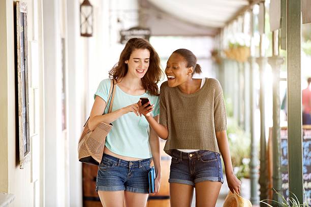istock Smiling young women walking together using mobile phone 533351672