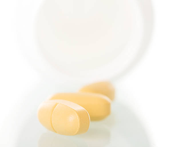 istock Yellow pills spilled from  bottle isolated on  white background 533352870