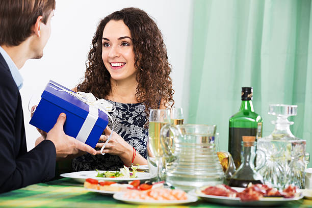 Man giving present to woman Man presenting gift to young woman during romantic dinner with champagne in home wonderingly stock pictures, royalty-free photos & images