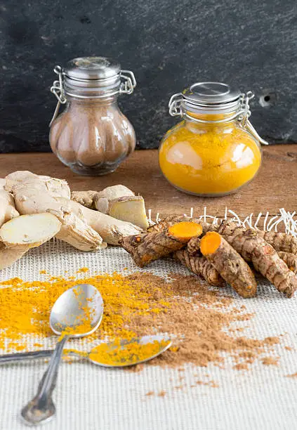 Healthy living begins with healthy food. Turmeric root and ginger root may help with anti-aging. Add to food, use as a tonic, or display a healthy lifestyle. Black background, classic spice jars, and ground curcumin and ginger with spoons