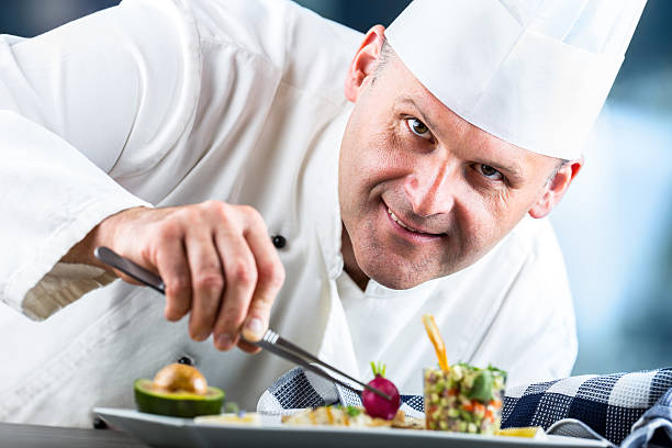 Chef in hotel or restaurant kitchen decorating dish with tweezers. Chef. Chef cooking.Chef decorating dish. Chef preparing a meal. Chef in hotel or restaurant kitchen prepares decorating dish with tweezers. Chef cooking, only hands. indoors restaurant hotel work tool stock pictures, royalty-free photos & images