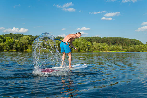 Young attractive man splashing water on stand up paddle board in the lake, SUP