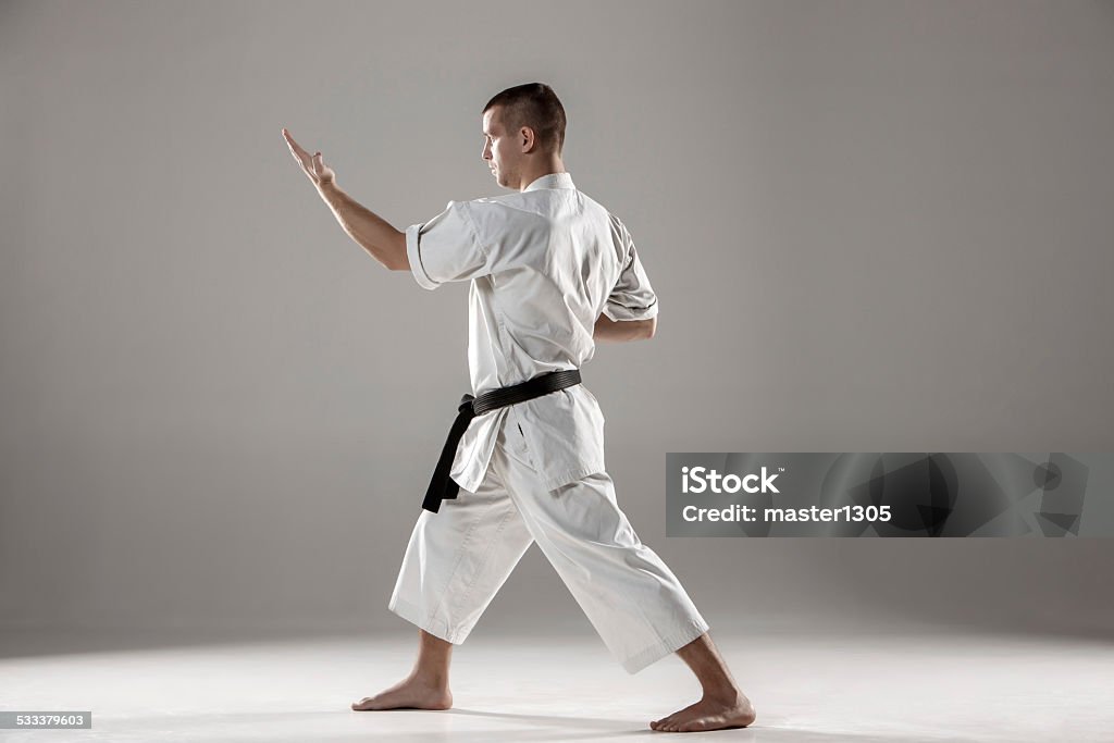 Man in white kimono training karate Man in white kimono and black belt training karate over gray background. 2015 Stock Photo