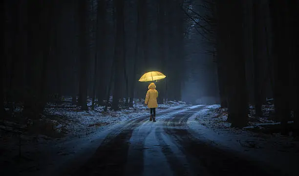 Little girl in the yellow coat with umbrella in the dark forest at night. Homage to Little Red Riding Hood