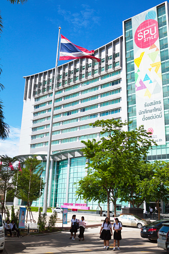 Bangkok, Thailand - July 12, 2013: Front building of Sripatum university seen from entrance to campus. A few students are passing campus. In center is pole with Thai flag. At facade is a huge banner.