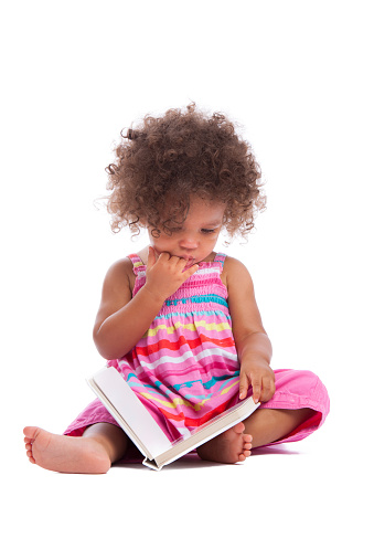 A portrait of a biracial baby girl/ toddler reading a book isolated on a white background.