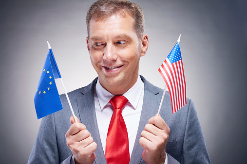 Man holding USA and EU flags, and looking at second one