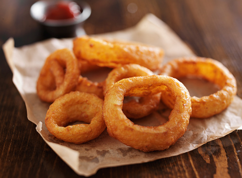crispy onion rings with ketchup on parchment paper close up and in horizontal composition