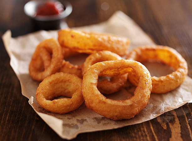 crispy onion rings close up crispy onion rings with ketchup on parchment paper close up and in horizontal composition fried onion rings stock pictures, royalty-free photos & images