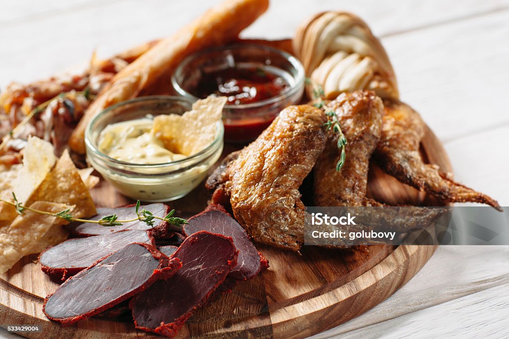 Meat beer snacks on white plate Meat beer snacks on white plate. Grilled chicken wings, pastirma, cheese and sauces top view. Close-up of beer snacks with focus on foreground Appetizer Stock Photo