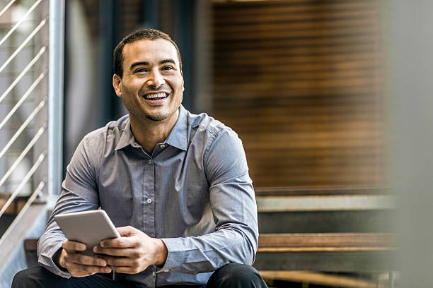 Happy businessman holding digital tablet A photo of happy businessman holding digital tablet. Professional is smiling while sitting on steps. Male in formals looking away. business man looking away stock pictures, royalty-free photos & images