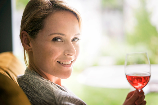 A portrait photo of beautiful woman having glass of red wine. Confident young female is celebrating with alcohol. Happy and relaxed lady is at home.