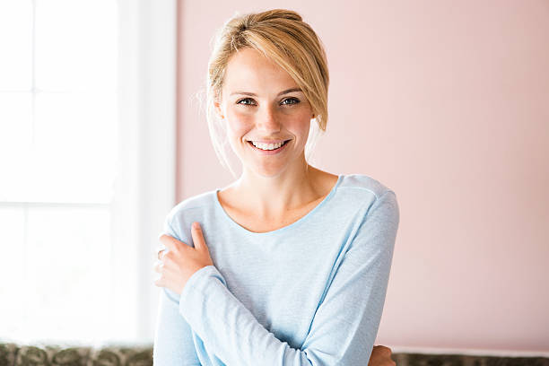 Portrait of smiling young woman at home Front view portrait of beautiful woman smiling at home. Young female is in casuals. Attractive lady is in brightly lit room. blond hair stock pictures, royalty-free photos & images