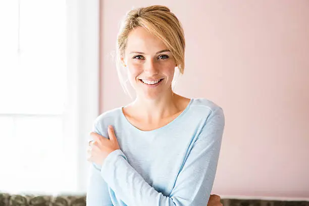 Front view portrait of beautiful woman smiling at home. Young female is in casuals. Attractive lady is in brightly lit room.