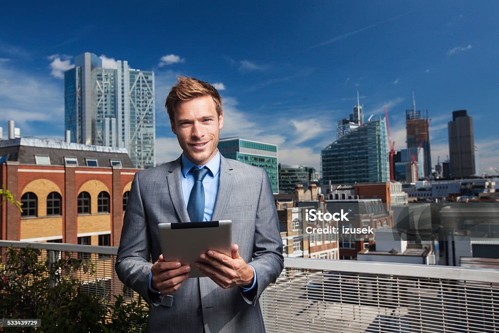 Outdoor portrait of businessman with digital tablet Outdoor portrait of professional businessman standing outside against cityscape with digital tablet, smiling at camera. 2015 Stock Photo