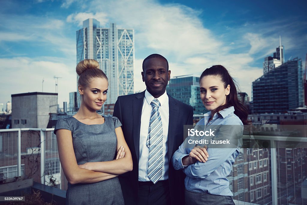 Outdoor Portrait of successful business people Three confident business people standing oustodoor on the rooftop with the city scape in the background. Heroes Stock Photo