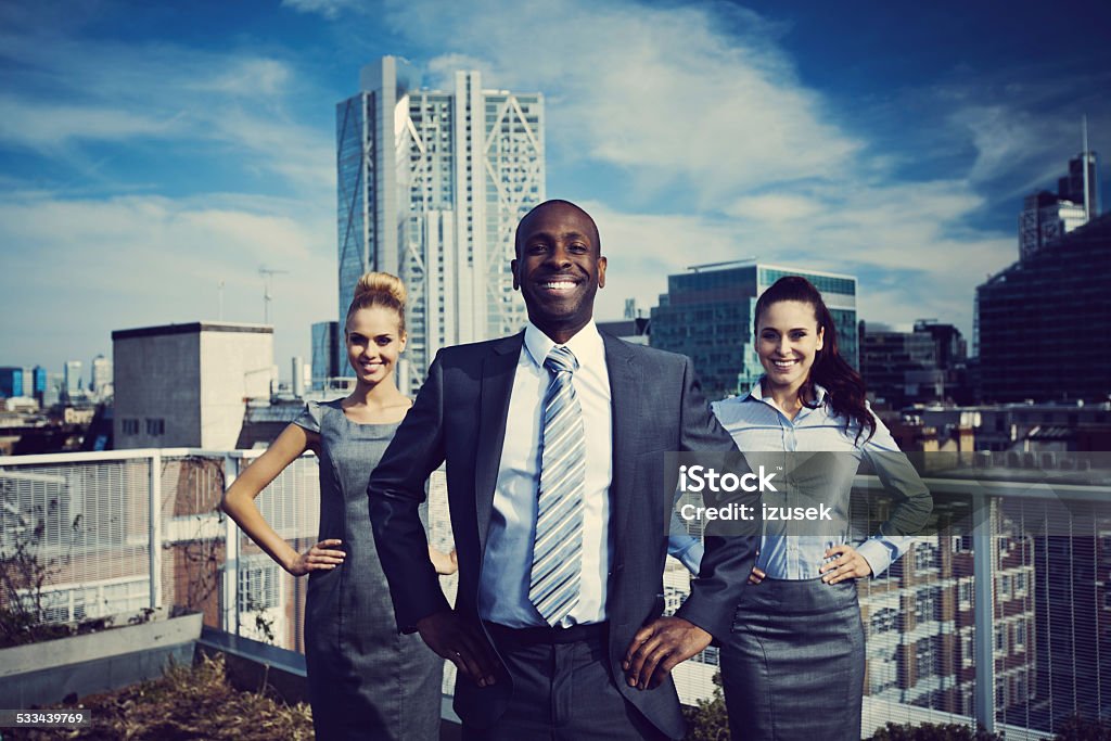 Business Superheroes standing outdoor on rooftop Three happy business people standing oustodoor on the rooftop with the city scape in the background. Heroes Stock Photo