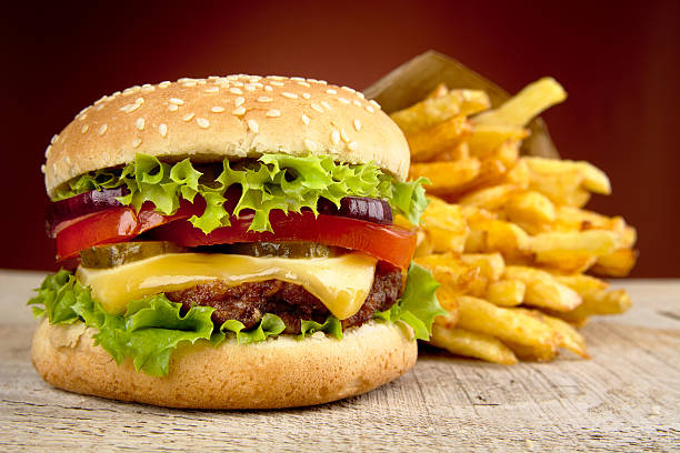 cheeseburger patatine fritte su rossa e riflettori su tavolo in legno - burger french fries cheeseburger hamburger foto e immagini stock