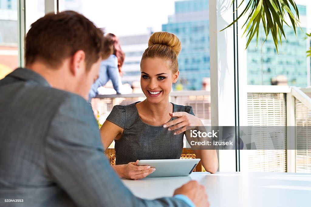 Businesswoman talking with her business partner Businesswoman having meeting ina an office with her business partner, holding digital tablet in hand. City scape in the background. 2015 Stock Photo