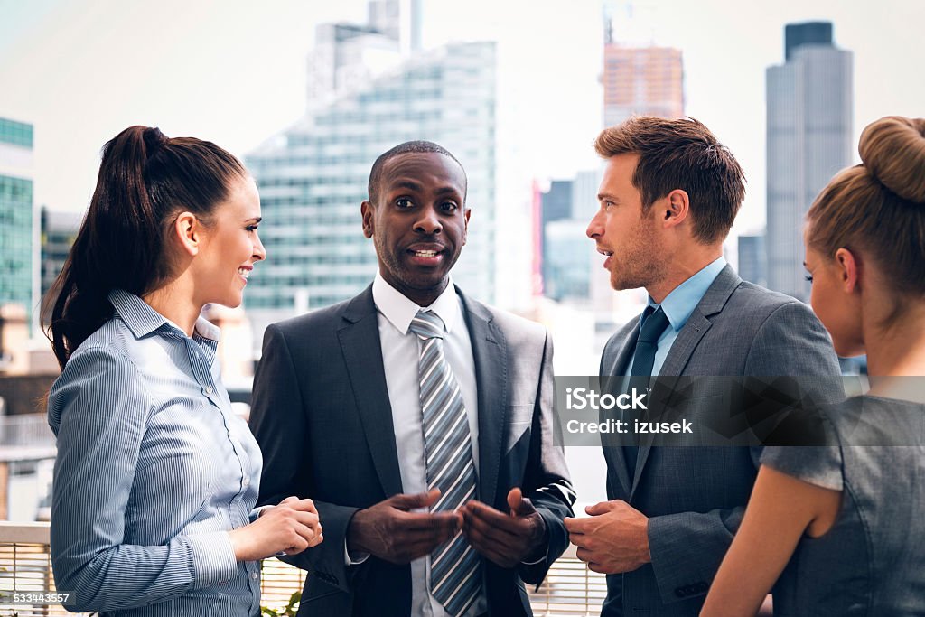 Business people discussing outdoor Group of happy business people talking outdoor with city scape in the background. Laughing Stock Photo