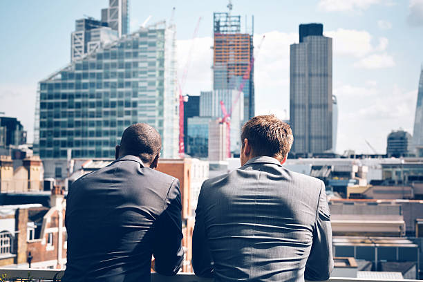 Two businessmen looking at city scape Back view of two businessmen - caucasian and afro american - standing outdoor and looking at city scape. financial occupation stock pictures, royalty-free photos & images