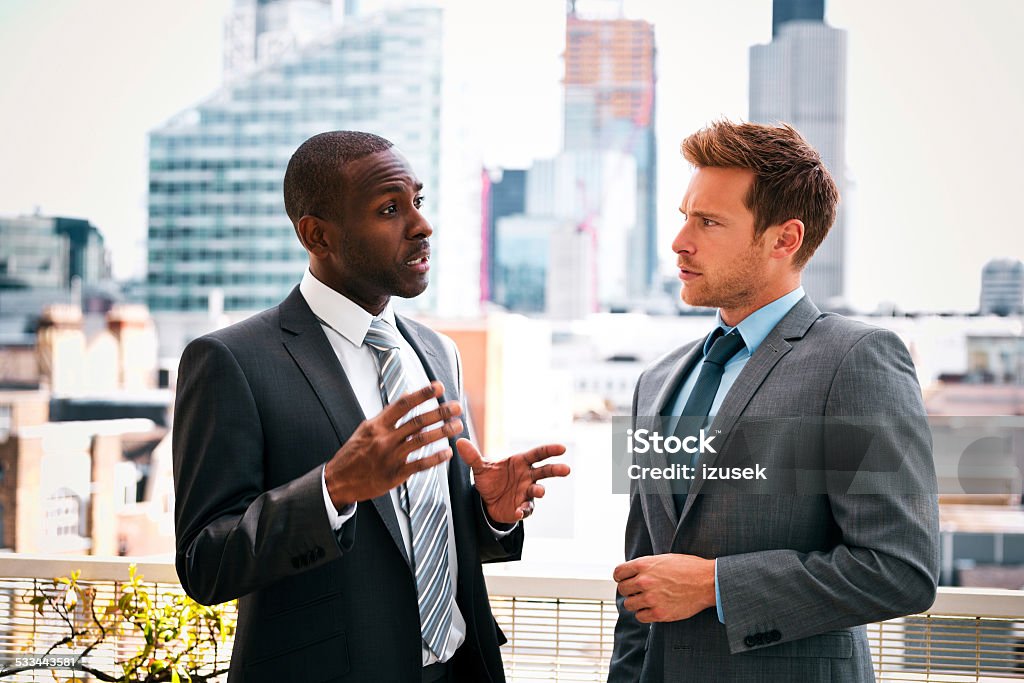Business people discussing outdoor Afro american businessman discussing with his business partner, standing outdoor with city scape in the background. Finance Stock Photo
