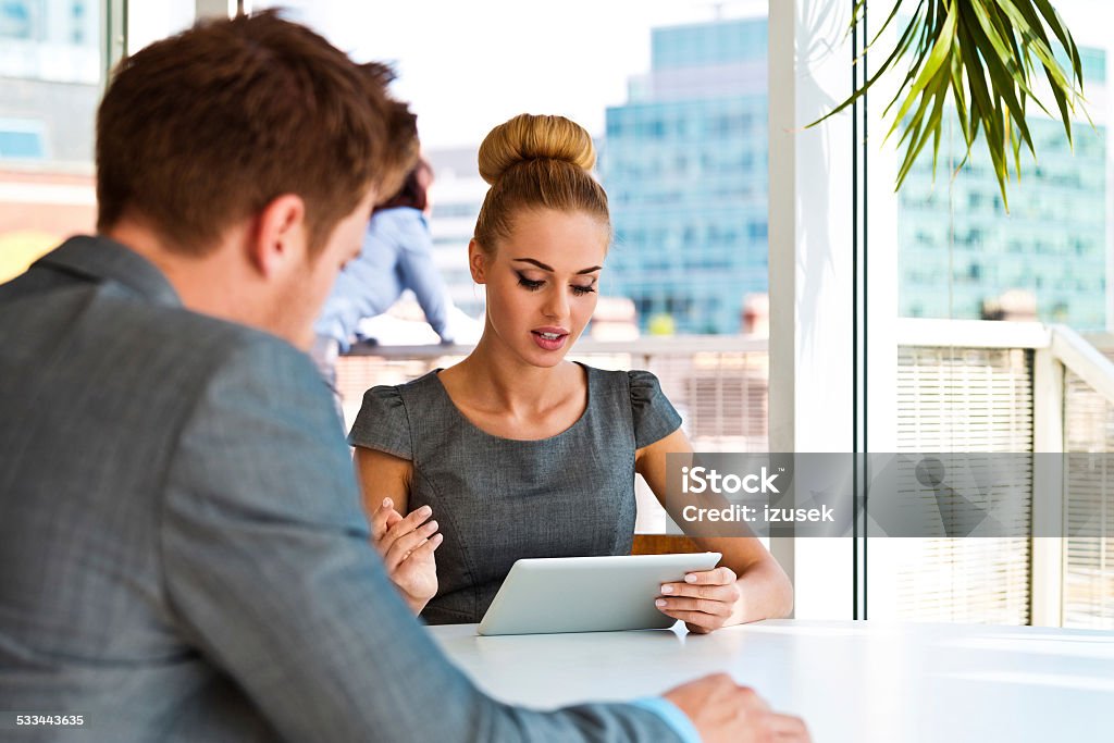 Businesswoman talking with her business partner Businesswoman having meeting ina an office with her business partner, looking at digital tablet. City scape in the background. Business Stock Photo