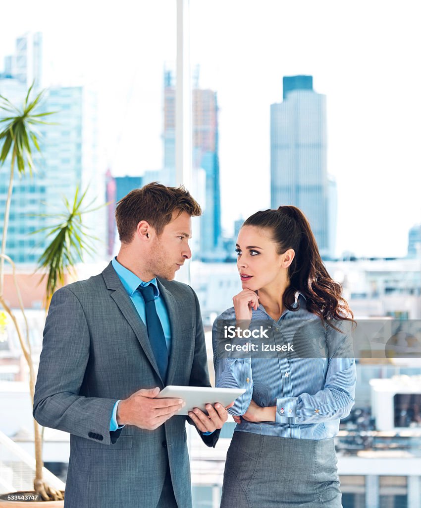 Business people discussing in an office Businesswoman and businessman talking in an office, man holding a digital tablet in hands, city scape in the background. 2015 Stock Photo
