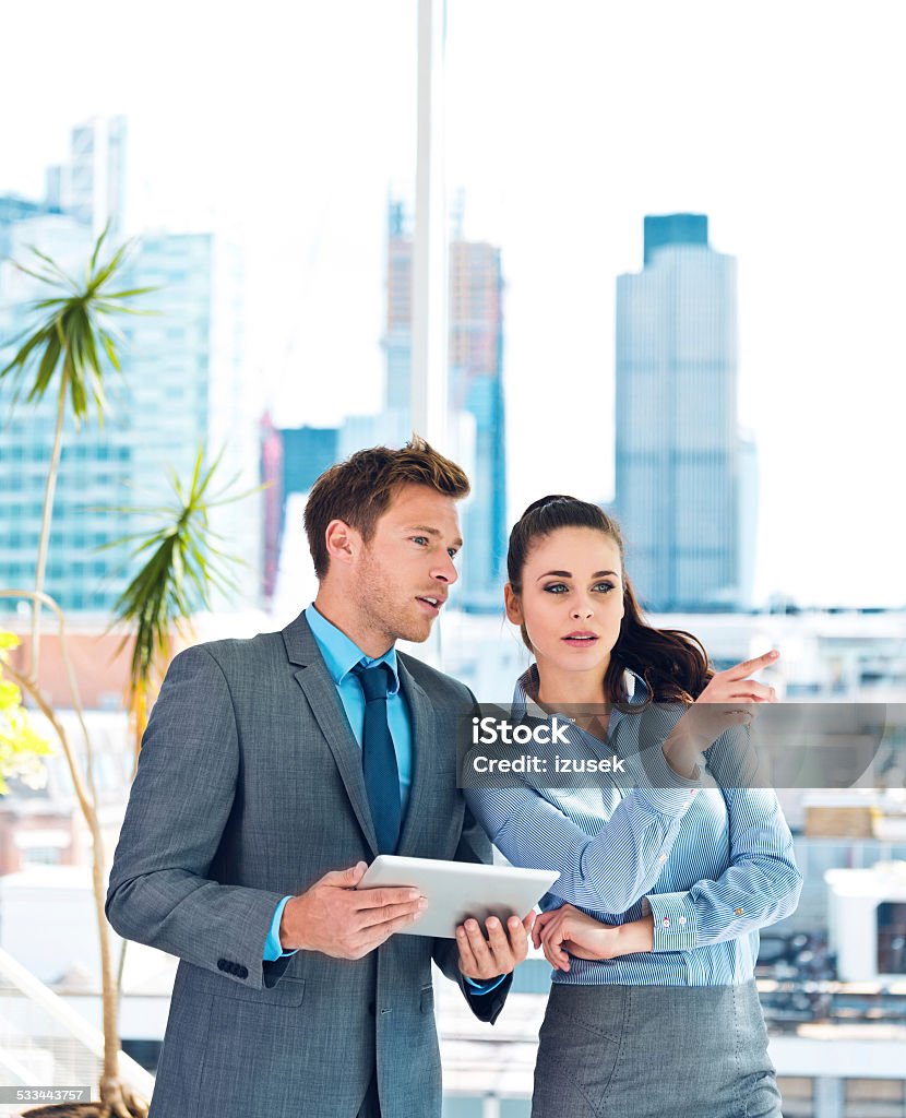 Business couple discussing in an office Businesswoman and businessman talking in an office, man holding a digital tablet in hands, city scape in the background. Real Estate Agent Stock Photo