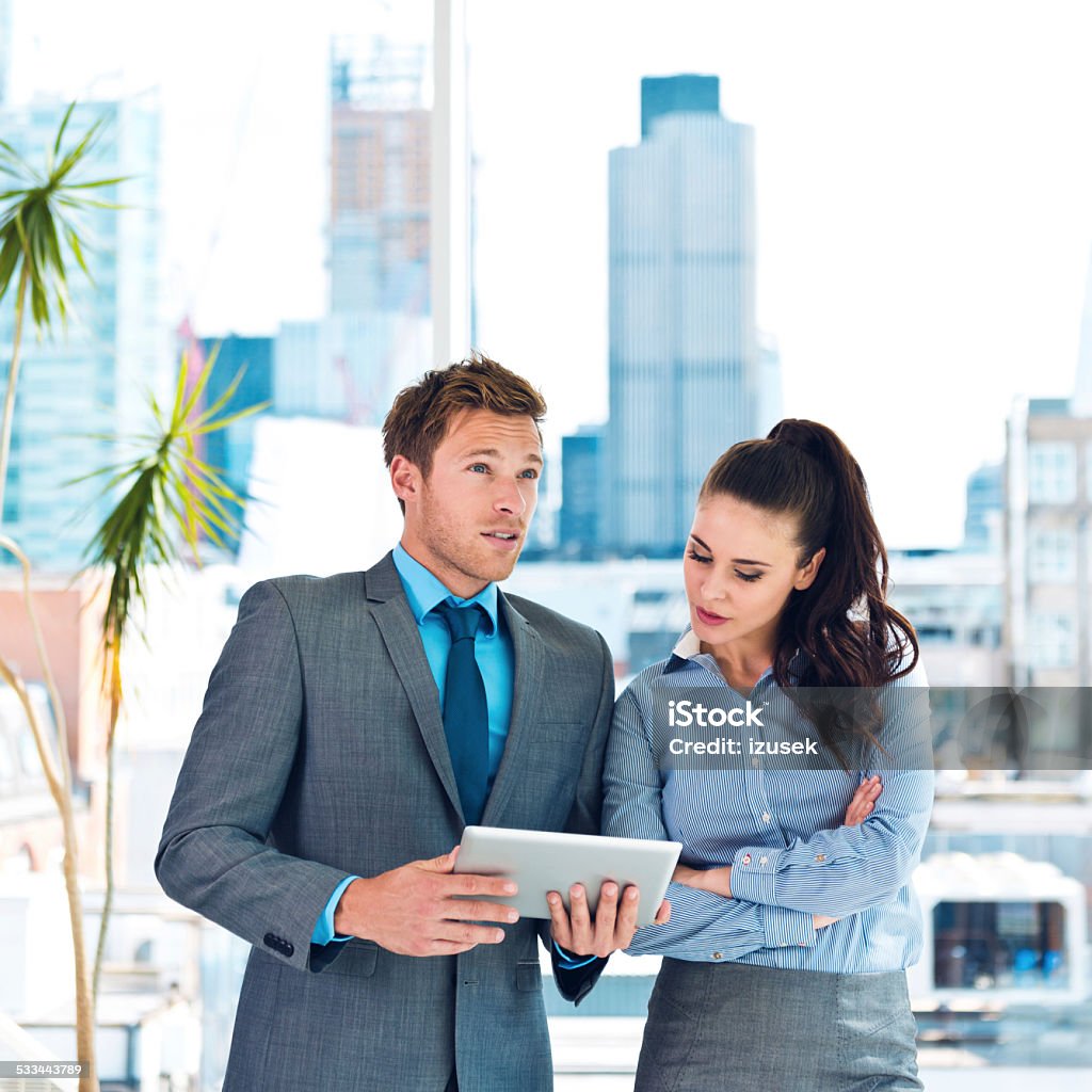 Business people discussing in an office Businesswoman and businessman talking in an office, man holding a digital tablet in hands, city scape in the background. Real Estate Agent Stock Photo
