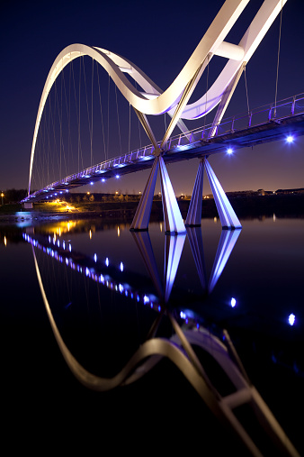 Night view showing a reflection of the Infinity Bridge, a public pedestrian and cycle footbridge across the River Tees in the borough of Stockton-on-Tees in the north east of England.