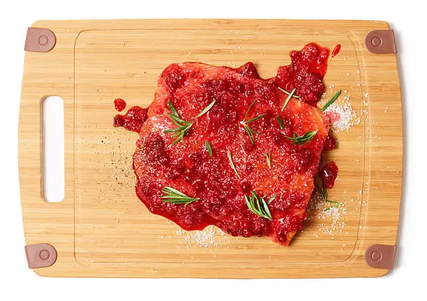 Salmon steak being marinated in salt with rosemary and redberries, isolated