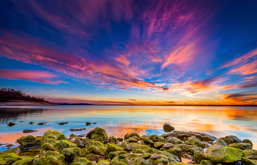 Amazing multicolored sunset over Benbrook Lake in Fort worth, TX featuring vivid green mossy rocks in the foreground