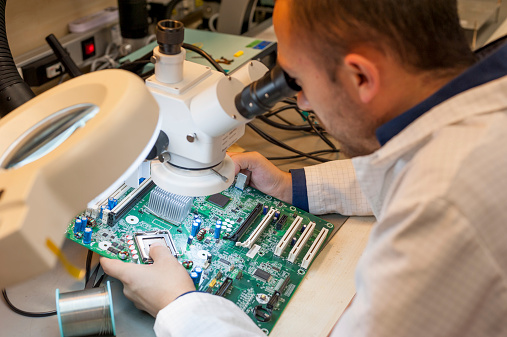An  electronic technician working on computer motherboard, inspection electronic connections and electronic parts with a microscope
