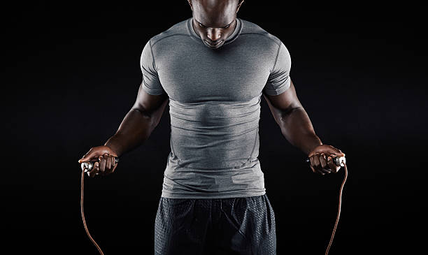 Muscular man skipping rope. Portrait of muscular young man exercising with jumping rope on black background