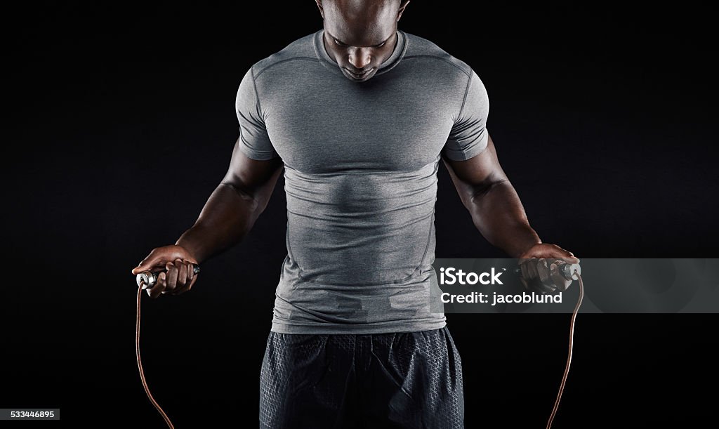 Muscular man skipping rope Muscular man skipping rope. Portrait of muscular young man exercising with jumping rope on black background Men Stock Photo