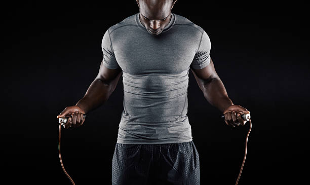 Muscular man skipping rope Muscular man skipping rope. Portrait of muscular young man exercising with jumping rope on black background sports clothing stock pictures, royalty-free photos & images