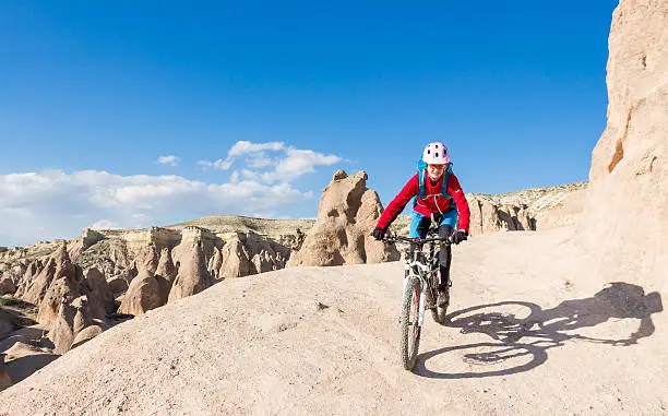 A female mountainbiker is riding on tuff formations nearby the City of Göreme, Cappadocia. The area is famous for its sedimentary rocks formed in lakes and streams and ignimbrite deposits that erupted from ancient volcanoes approximately 9 to 3 million years ago. The rocks of Cappadocia near Göreme eroded into hundreds of spectacular pillars and minaret-like forms. 