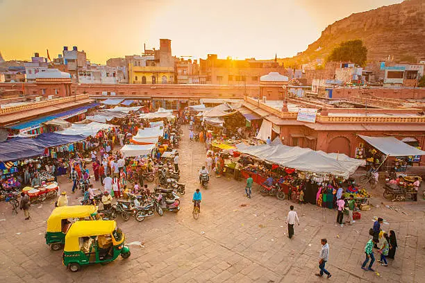 The beautiful market in Jodhpur’s Old City. People are visible in the image, walking standing or sitting in their rickshaws as it is the case in the foreground.