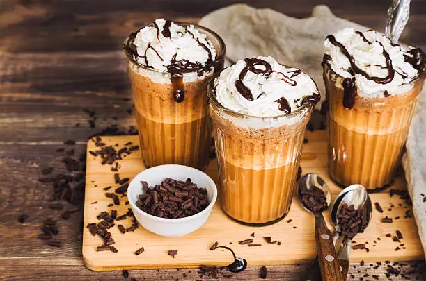 Homemade coffee cocktail with whipped cream and liquid chocolate on rustic wooden background