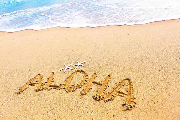 The Hawaiian greeting of hello "aloha" written on the sandy beach of Hawaii, greeting vacationers to the islands.