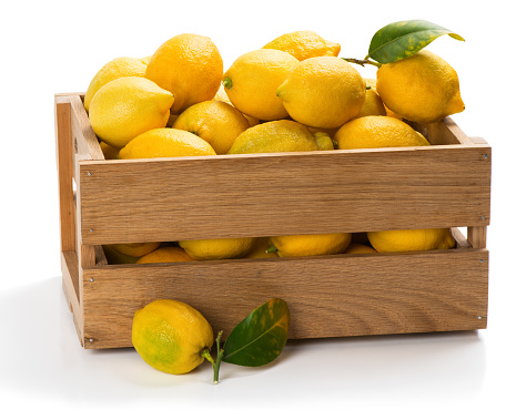 Lemons with green leaves in a crate with one on the surface in the foreground isolated on white background.